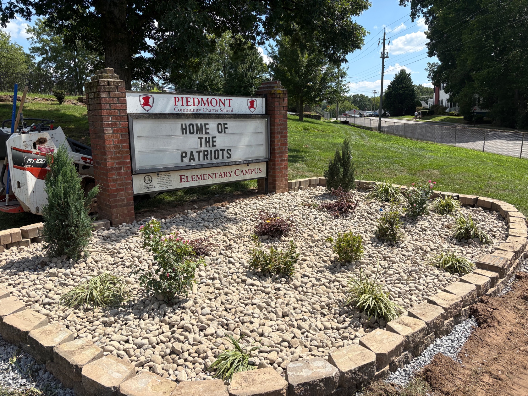 River rock planting bed with junipers, roses and ornamental grasses inside a block border around a school entrance sign in Gastonia, NC