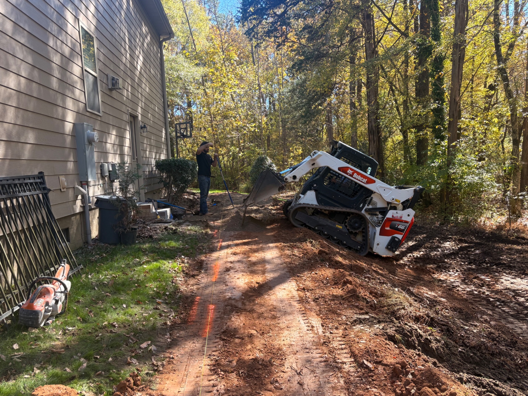 Skid steer excavating a marked drainage trench line along the side of a house before pipe installation in Mooresville, NC