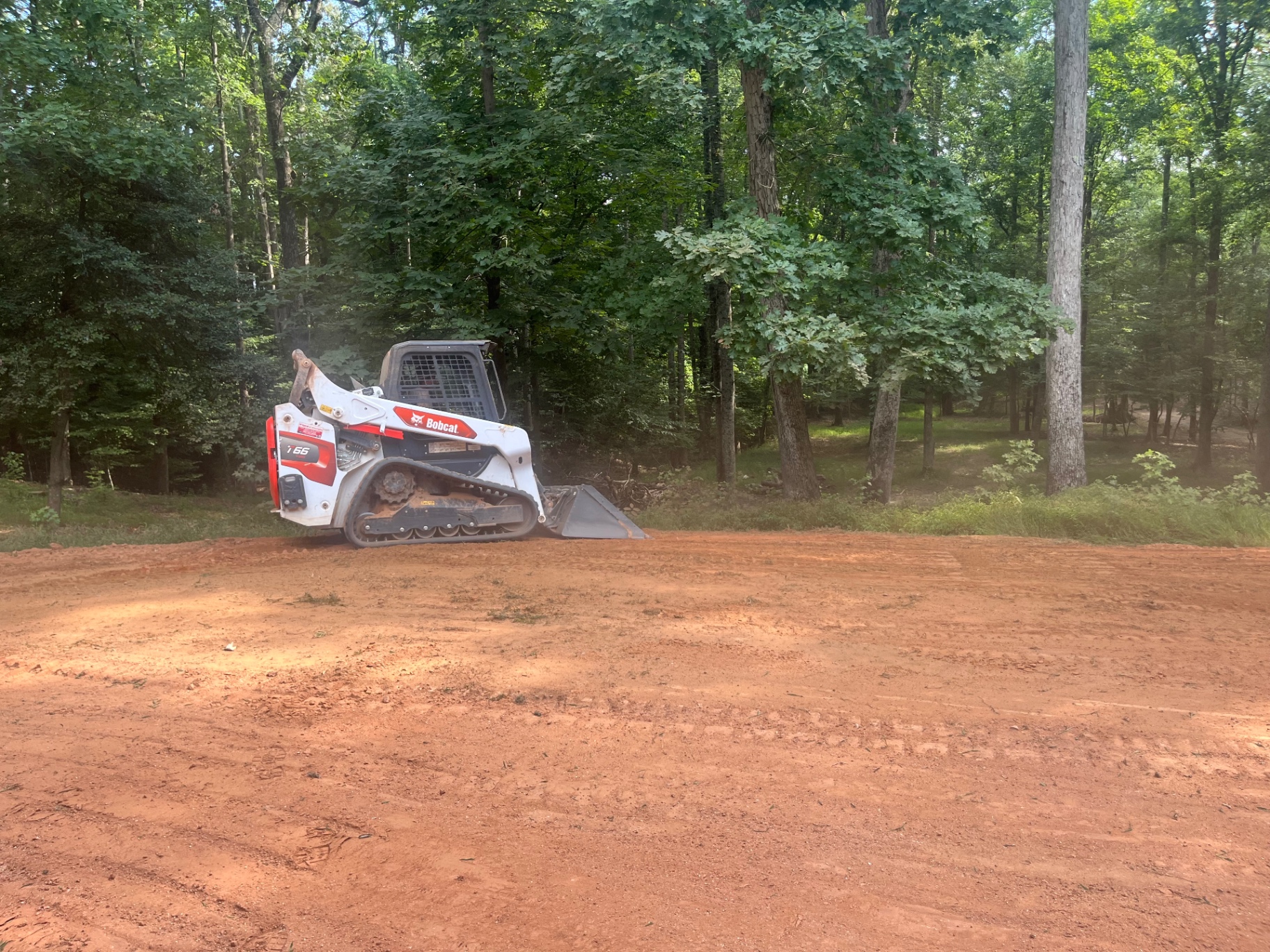 Track loader grading a freshly cleared red-clay lot at the edge of the woods in Cherryville, NC