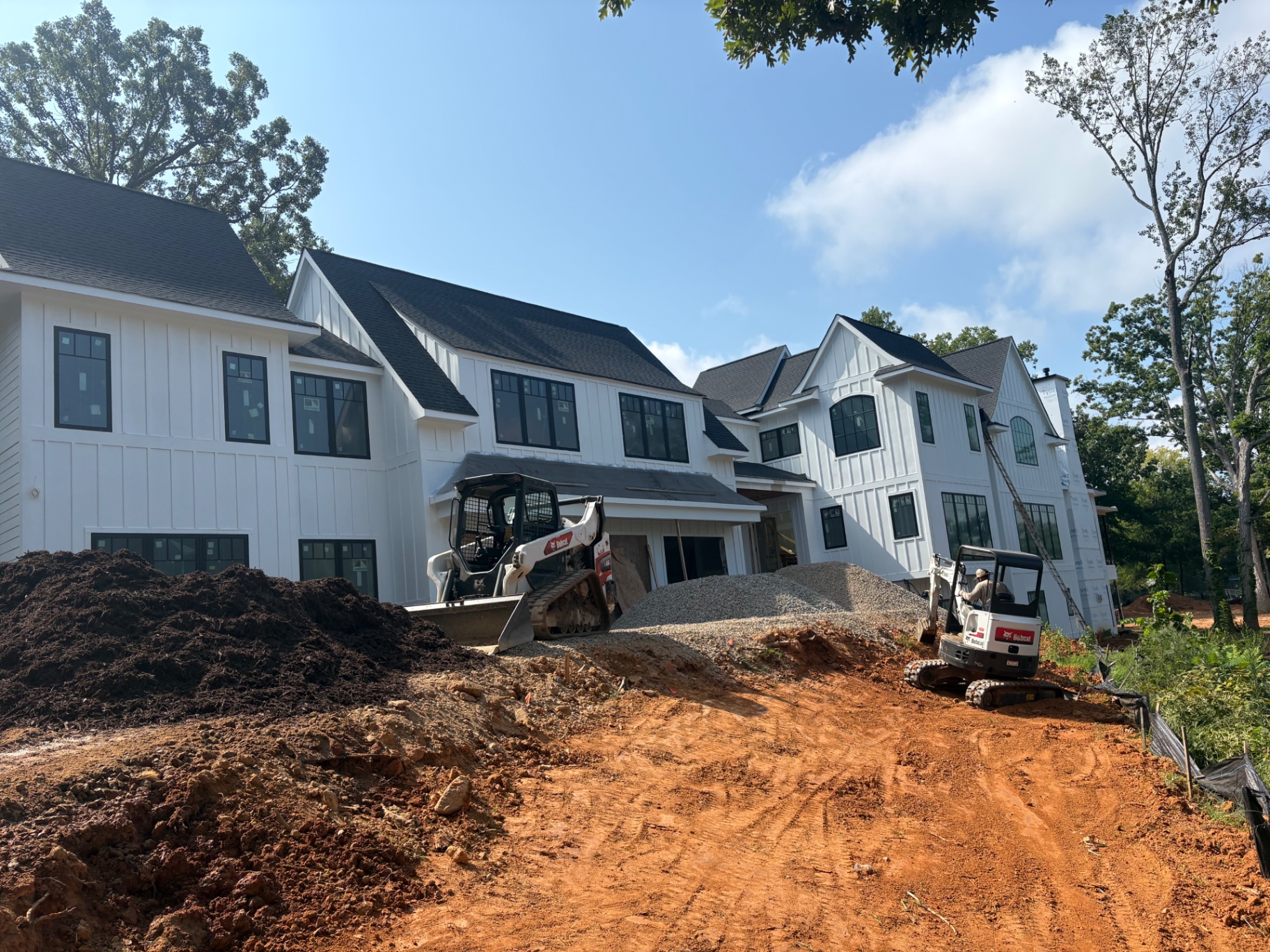 Skid steer and compact excavator completing site grading around a newly constructed Lake Norman area home