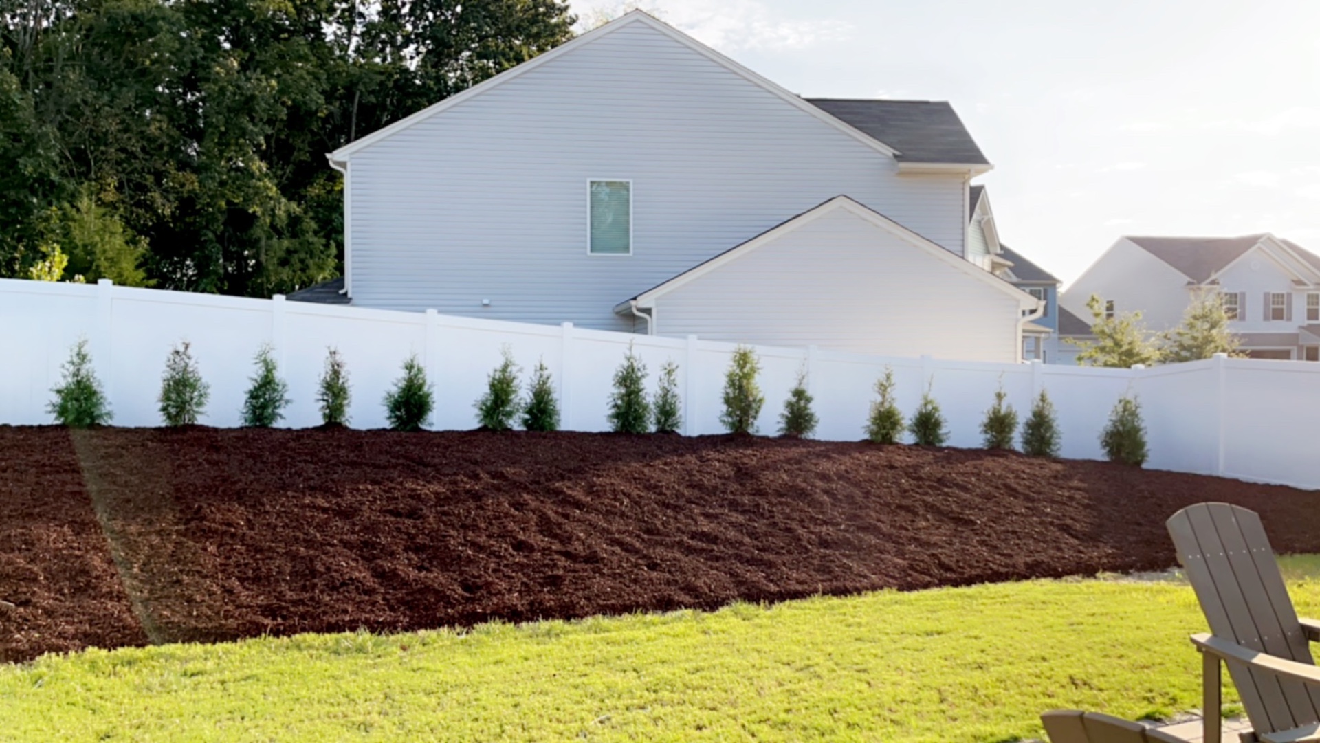 Newly mulched sloped backyard bed with a row of young arborvitae along a white privacy fence in Mt. Holly, NC
