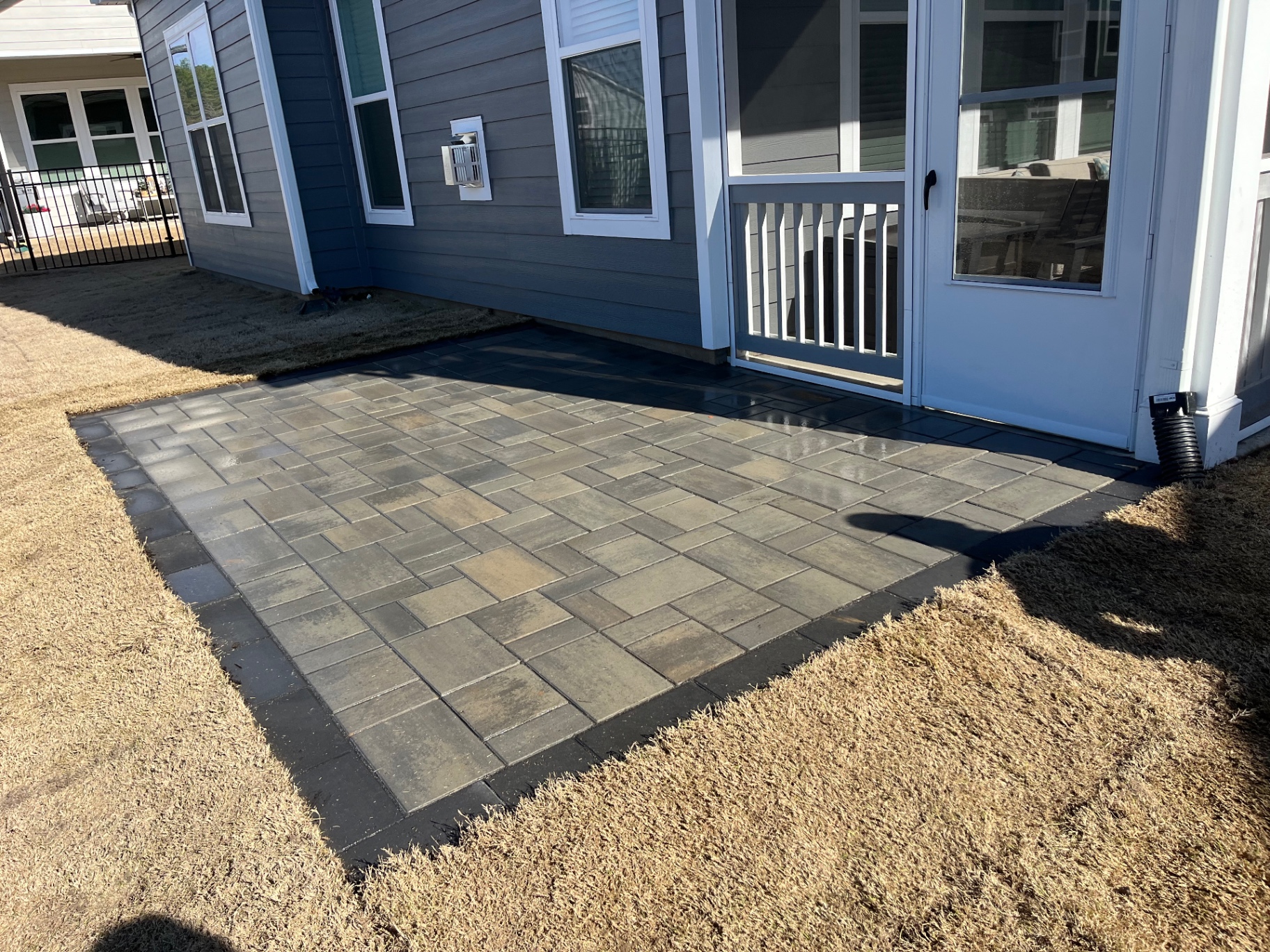 Gray multi-tone paver patio with charcoal border course beside a screened porch on a Denver, NC home