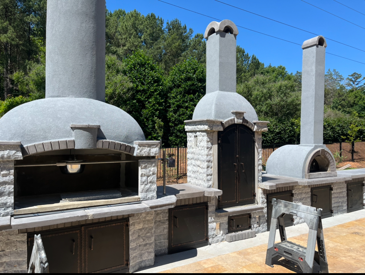 Masonry outdoor kitchen with wood-fired oven and chimneys on a paver patio, Mooresville NC