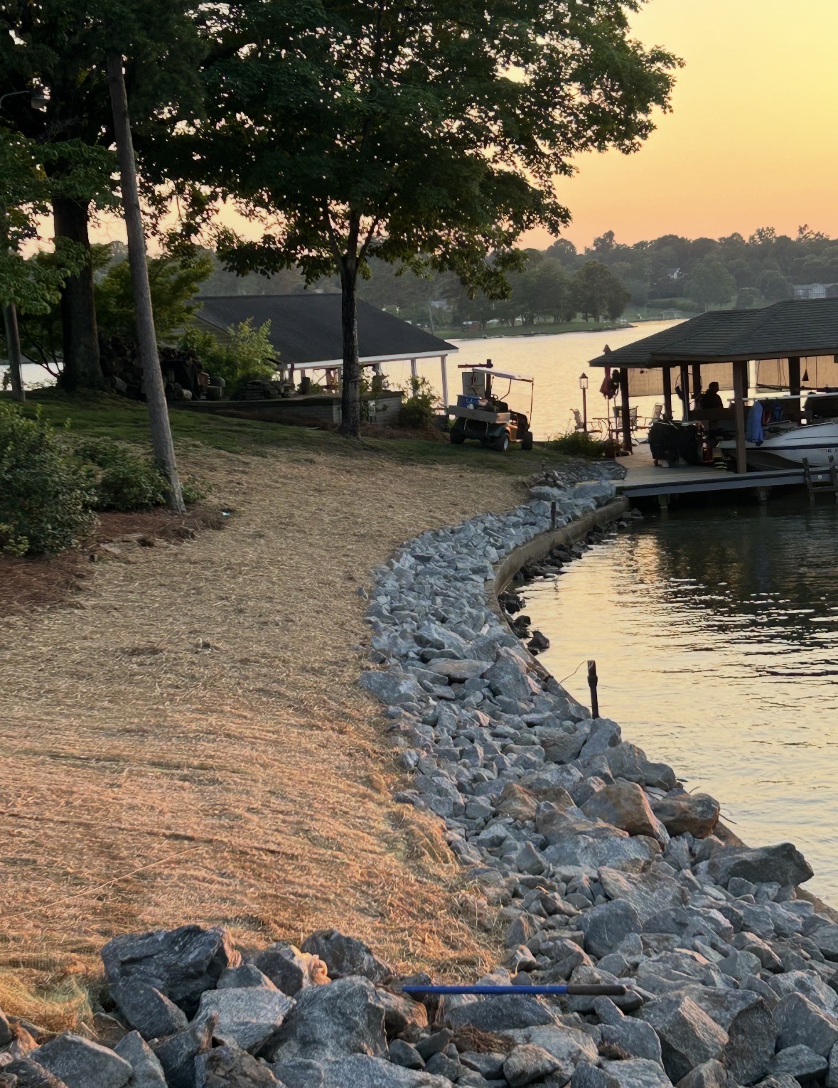 Rip rap rock shoreline stabilization along a Lake Norman waterfront at sunset with a dock and boathouse