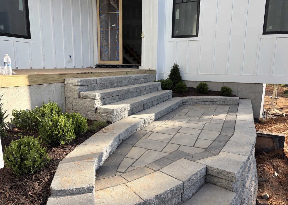 Light gray paver patio with dark soldier-course border, block retaining walls and wide steps leading to a house entrance in the Lake Norman area